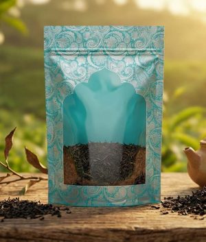 چای ممتاز گیلان ۲۰۰ گرمی در بسته‌بندی پاکت ترک‌دار با پنجره شفاف، کنار قوری سفالی در باغ چای
